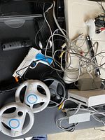 Table surface with two white Wii steering wheels, white Nunchuk, composite cables, sensor bar and adapters