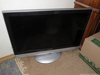 37-inch Mitsubishi flat screen television with silver base stand and black screen showing some reflections. The TV displays minor signs of cosmetic wear but appears clean and intact.