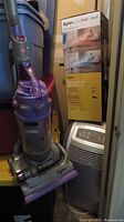 Dyson upright bagless vacuum cleaner in grey and purple alongside Dyson Pure Hot+Cool box and silver portable air conditioner