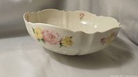 Side angle of ivory serving bowl with pink and yellow rose floral design and scalloped trellis shape.