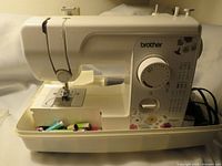 Front side view of Brother JX-2517 sewing machine showing stitch selection dial, needle area, accessory compartment with sewing threads.