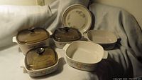 Front view showing 3 casserole dishes with amber Pyrex lids and 1 casserole dish without lid, plus a floral patterned dinner plate in background