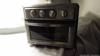 Front view of the stainless steel Cuisinart convection airfryer toaster oven showing four control dials, oven door with handle and glass window, set on a white surface.