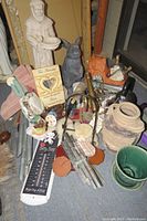 Photo of St Francis statue, gray ceramic bunny statue, orange cement bird, other items including pots and wind chimes on floor.