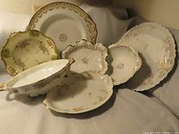 Group shot of seven vintage Limoges porcelain platters and plates with floral patterns and gold trim, showing variety of shapes and sizes.