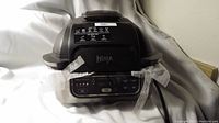 Front view of Ninja Foodi 5-in-1 Indoor Grill showing control panel, black and silver body, and Ninja logo on the lid.