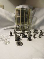Photo of 2 crystal roosters, 1 crystal whale, and 19 pewter animal and human figurines arranged in front of a mirror-backed glass display case.