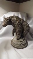 Front and side view of the brown bear bust sculpture on round base, showing detailed fur texture and form.