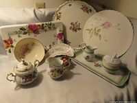 Photo of various china plates, cream and sugar sets, and decorative items with floral rose patterns, showing overall lot contents.