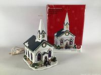 Lighted wedding chapel with green wreaths and painted details beside original red box with snowflake design, showing overall lot condition and packaging.