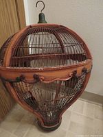 Front side view of the wooden hot air balloon bird cage showing detailed wooden frame, wire bars, and metal hook on top.