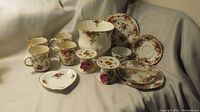Full set of Royal Albert Old Country Roses pieces arranged showing jardiniere, mugs, plates, heart dish, and pedestal dishes with floral designs and gold trim.