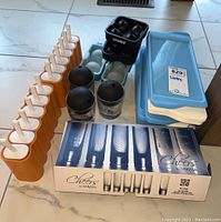 Lot contents showing a set of orange plastic popsicle molds, plastic blue ice cube trays, Flamen ice ball molds, two textured glasses with lids, and boxed Mikasa Cheers shot glasses.