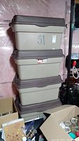 Four stacked Rubbermaid plastic storage boxes with lids, beige with brown lids and writing 'S1' on sides.