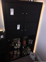 Front view of black cabinet showing four top doors and four open shelves below with various jars and containers inside the cubbies.