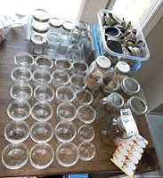 Overhead view of canning jars arranged on a wooden table alongside two bins of metal canning lids and sheets of canning labels.