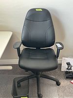 Full view of black office chair sitting on clear floor mat with a small black trash bin next to the chair base.