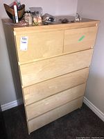 Front view of the six-drawer light wood dresser with various small items on top.