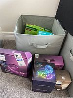 Grey fabric bin containing assorted smart lighting boxes including Philips Hue and Govee products