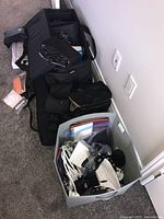Multiple gear items in black bags and a grey bin: cables, boxes, stands