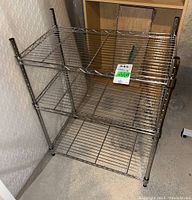 Front angled view of the metal shelving unit showing three wire shelves and four vertical posts with black caps.