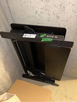 Folded black VIV standing desk propped against a wall, showing metal frame and lifting mechanism