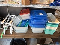 Stack of Made Smart large bins in white and teal/light blue, clear bins with assorted lids, and white plastic rack for tins.