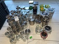 Wide view of varied glass and plastic jars with metal lids clustered on floor showing approximate quantities and styles
