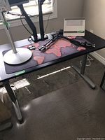 Full view of office table with a black top featuring a world map desk mat and silver metal legs.
