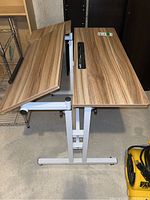 Photo showing the desk with tilted wood veneer top section and adjacent flat wood veneer section mounted on white metal frame base.