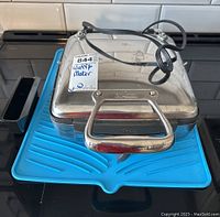 Closed waffle maker on blue silicone pad with power cord