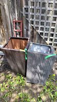 Two rectangular synthetic wicker patio planters side by side on dirt ground outdoors showing weathered condition.