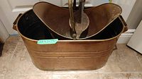 Rectangular copper bucket with handles and fireplace bellow inside, shown on tiled floor