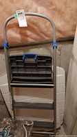 Photo of 3-step folding step stool ladder in untested condition, showing metal frame, curved handle, and plastic steps.