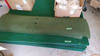 Stack of three green driving mats next to cardboard box of rubber tee holders