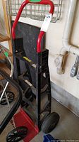 Full view of the heavy duty hand truck showing the red handle, black frame, and red base plate with large rubber wheels.