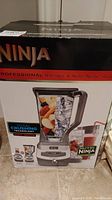 Box for Ninja Professional Blender and Nutri Ninja cups with product images and branding, showing blender with fruits and ice inside clear container, control panel, and Nutri Ninja cups.