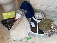 Photo of the bathroom scale, hair dryer, bath mat, neck pillow and cushions on tile floor.