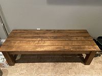 Front view of the wooden table or bench showing slatted top and thick legs