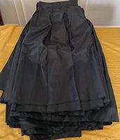 Stacked black table skirts laid on a yellow surface, showing pleated fabric and overall length.
