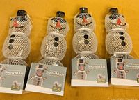 Four sealed white mesh snowman bird feeders on a yellow surface showing product tags and design details