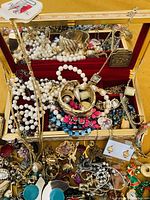 Photo of large lot showing multiple pieces of vintage jewelry inside and outside a vintage musical jewelry box with gold-tone exterior and red velvet interior liner.