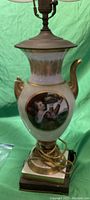 Porcelain and brass table lamp showing figurative design of a person playing a wind instrument, fabric lampshade, and brass fittings, image 1