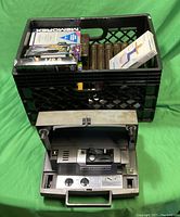 Vintage Kodak metal movie projector with knobs and handle in front of a black milk crate filled with assorted VHS and video tapes