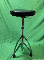 Front view of vintage Pearl drum throne showing black padded seat and chrome adjustable tripod legs with rubber feet.