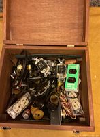Photo showing vintage wooden box filled with assorted electrical components such as sockets, outlets, wiring, switches, plugs, and metal plates.