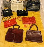 Photo showing eight women handbags in different colors and materials arranged on a yellow cloth.