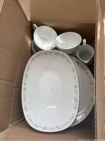 Top down view of box with white Noritake china pieces including a large oval serving plate and several cups and saucers