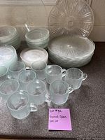 Photo showing frosted glass mugs, bowls, and serving platter with textured design on kitchen counter.