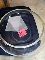 Photo of clear glass decorative bowl seen from top angle showing inside and smooth rim. Sticky note inside reads 'Lot 24 Glass Bowl'.